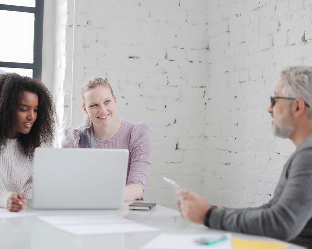 Two women on their laptop sitting across the table from an expert